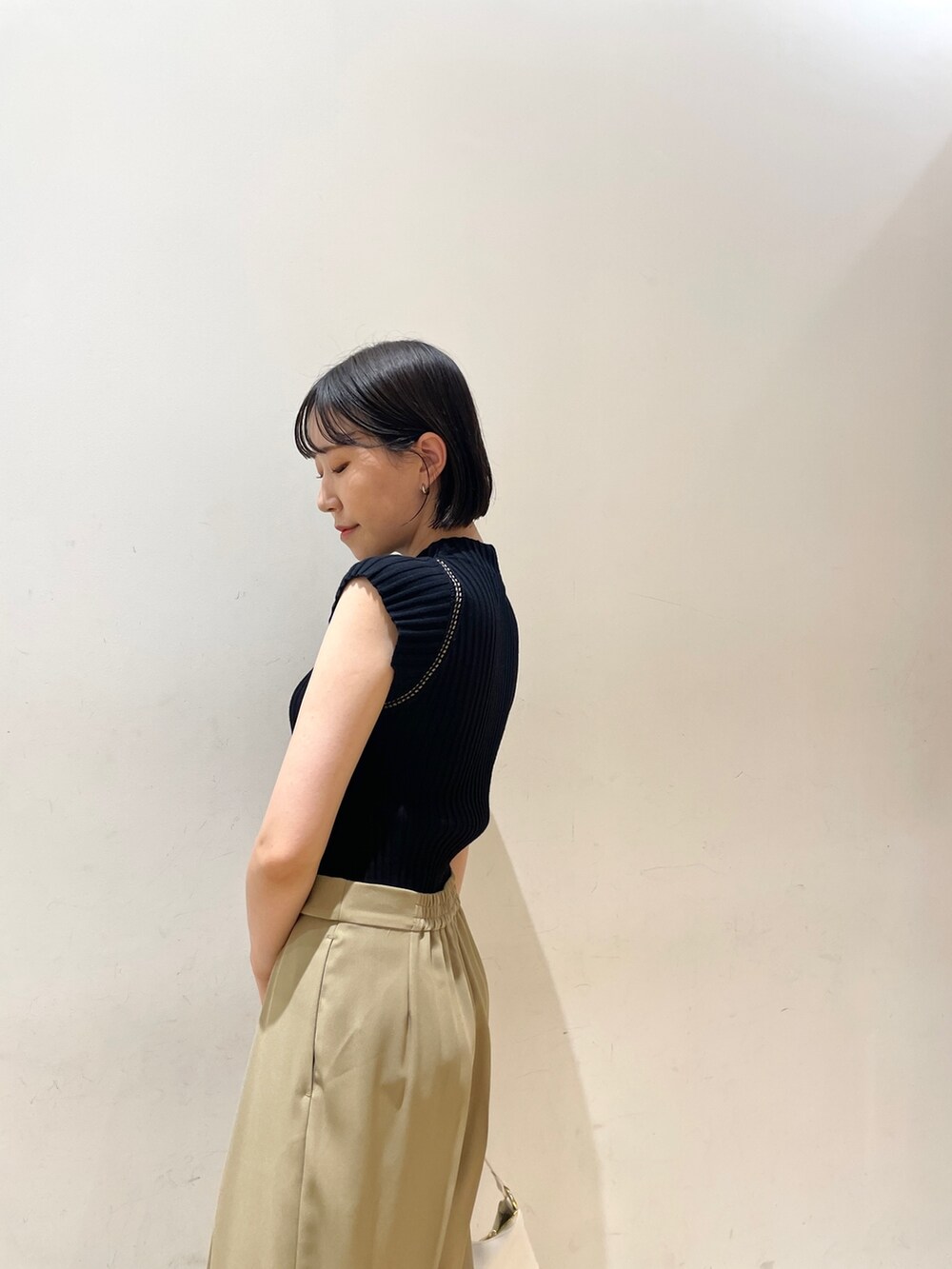 ブラック系のニット/セーター、ベージュ系のスラックス、ホワイト系のハンドバッグを着用したレディースの夏コーディネートの6枚目の写真