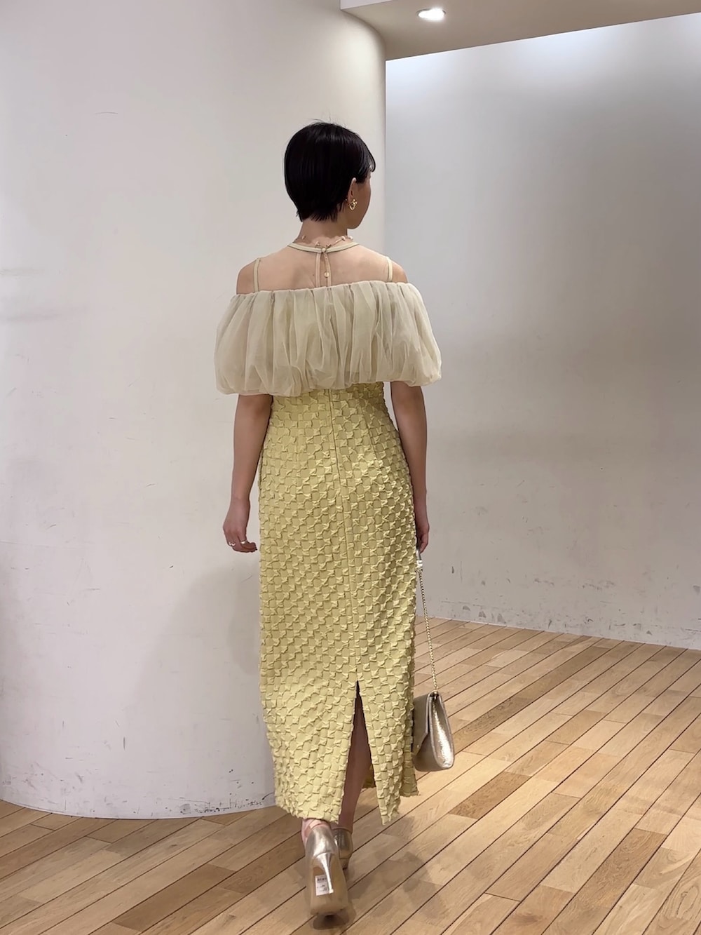 イエロー系のドレス、ゴールド系のパンプス、ゴールド系のクラッチバッグを着用したレディースの春コーディネートの4枚目の写真