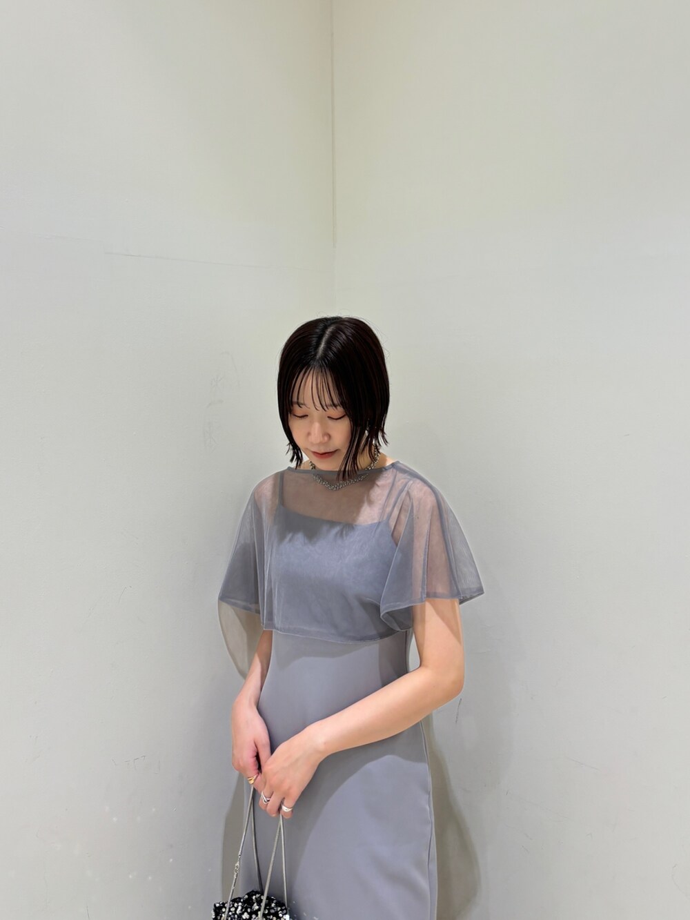 シルバー系のハンドバッグ、ブラック系のパンプス、パープル系のドレスを着用したレディースの夏コーディネートの4枚目の写真