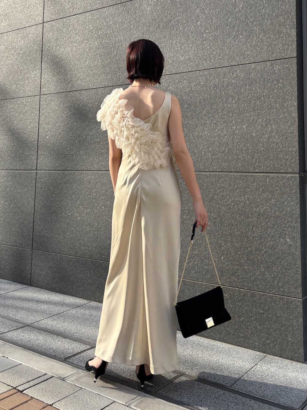 イエロー系のドレス、ブラック系のハンドバッグ、ブラック系のパンプスを着用したレディースの冬コーディネートの2枚目の写真