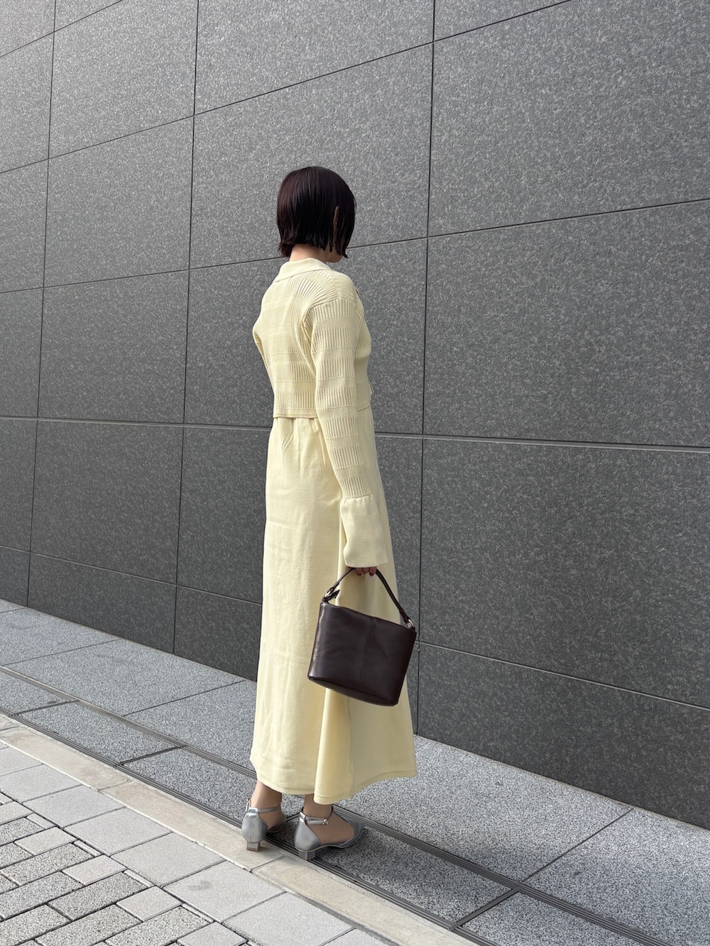 イエロー系のワンピース、ブラウン系のハンドバッグ、シルバー系のパンプスを着用したレディースの冬コーディネートの3枚目の写真