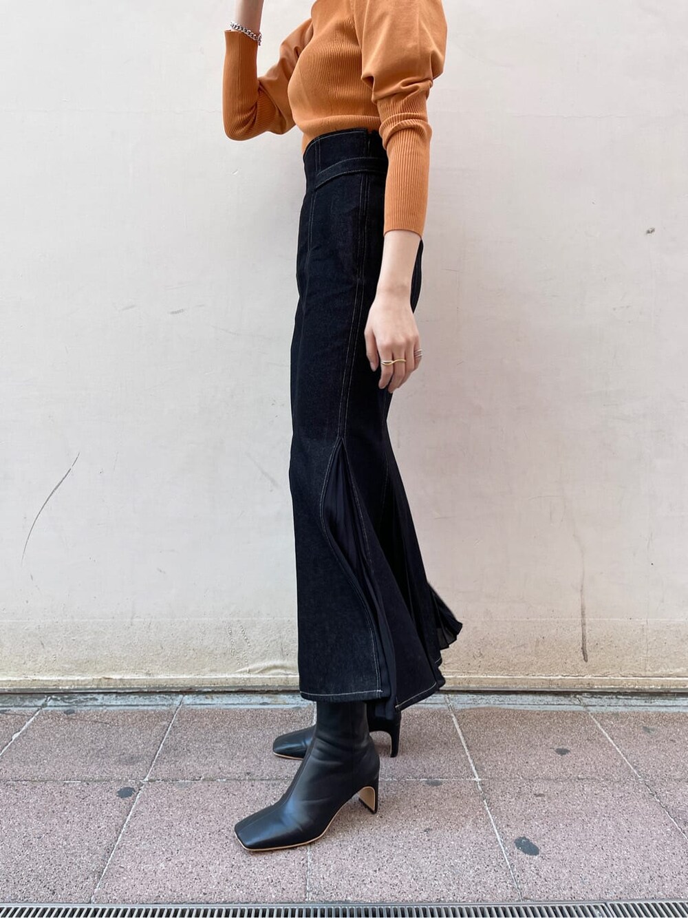 ブラック系のその他シューズ、オレンジ系のニット/セーター、ブラック系のスカートを着用したレディースの冬コーディネートの3枚目の写真