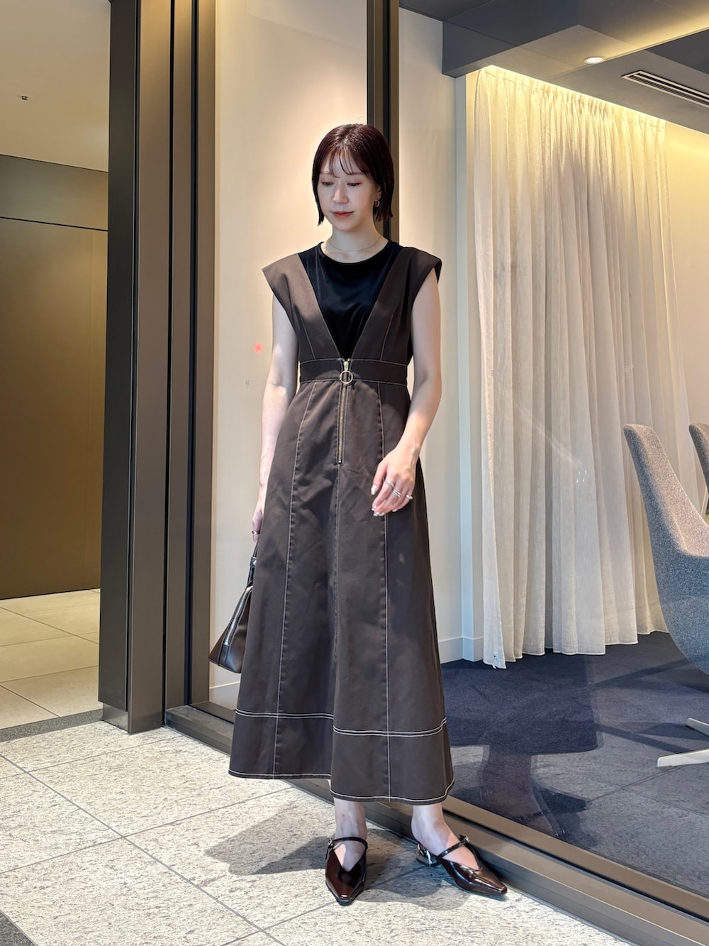 ブラウン系のジャンパースカート、ブラウン系のパンプス、ブラウン系のボストンバッグを着用したレディースの夏コーディネートの2枚目の写真