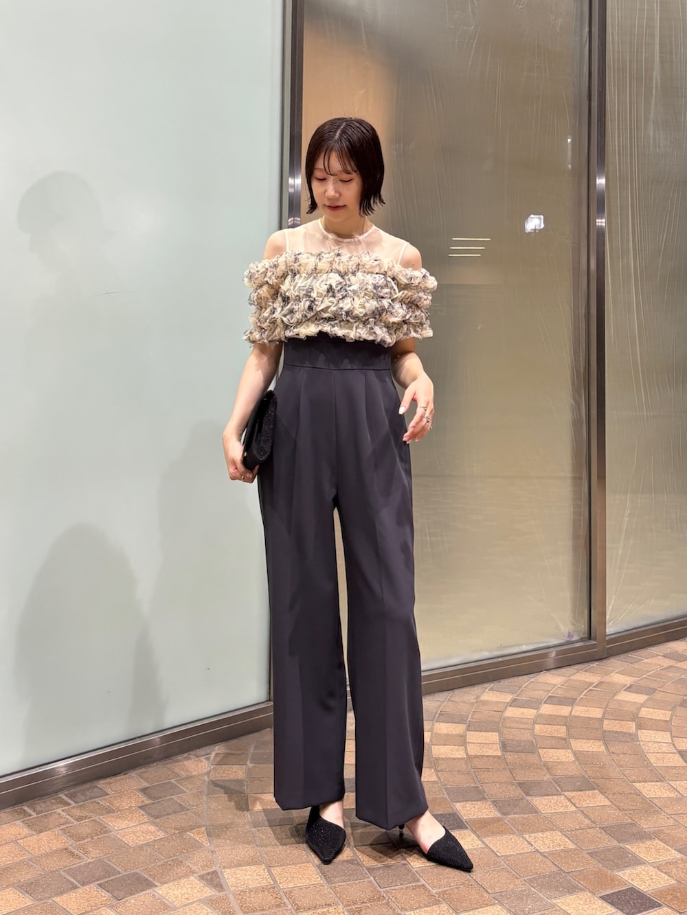 グレー系のパンツドレス、ブラック系のクラッチバッグ、ブラック系のパンプスを着用したレディースの夏コーディネートの3枚目の写真