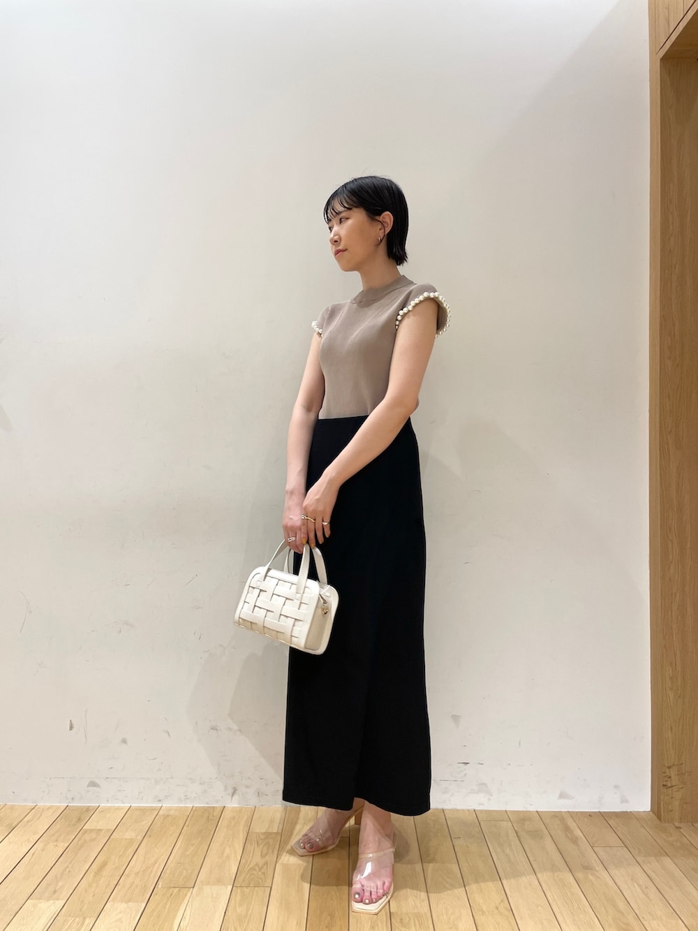 ブラック系のスカート、ベージュ系のニット/セーター、ホワイト系のショルダーバッグを着用したレディースの夏コーディネートの2枚目の写真