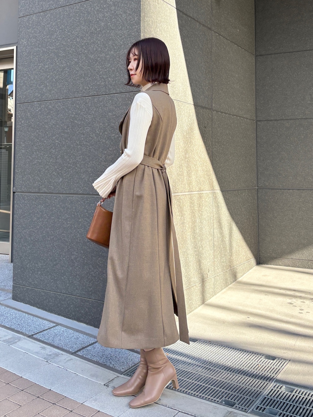 ブラウン系のワンピース、ホワイト系のニット/セーター、イエロー系のハンドバッグを着用したレディースの冬コーディネートの2枚目の写真