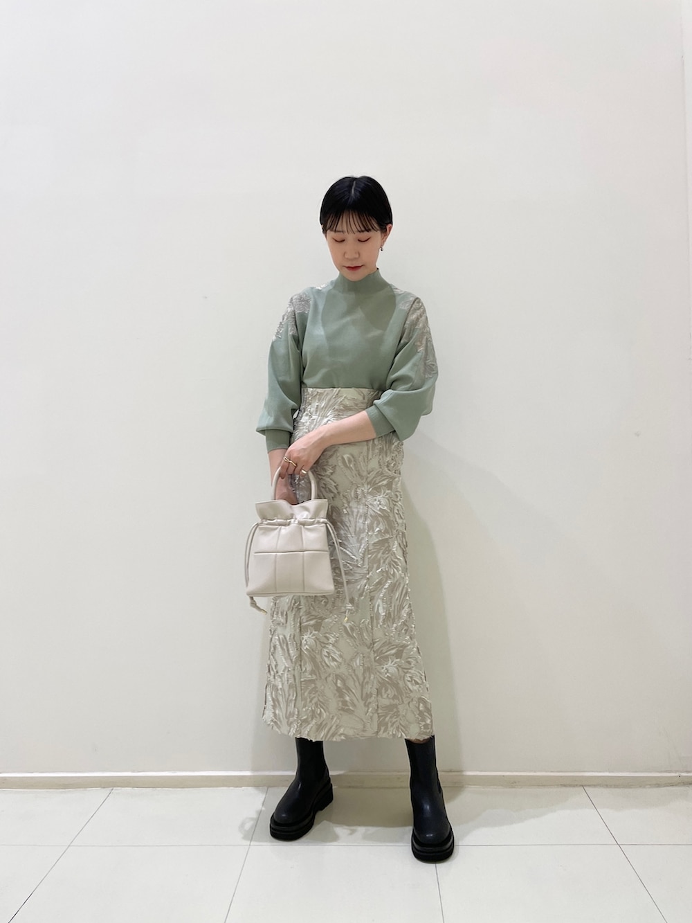 ベージュ系のスカート、グリーン系のニット/セーター、ホワイト系のハンドバッグを着用したレディースの冬コーディネートの2枚目の写真