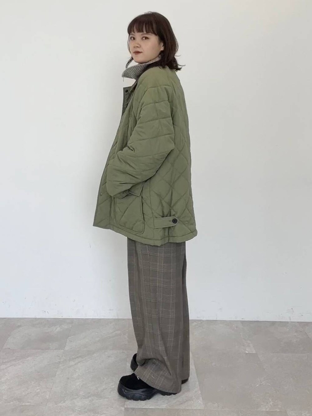 グリーン系のブルゾン、ブラウン系のスラックス、ベージュ系のニット/セーターを着用したレディースの秋コーディネートの2枚目の写真