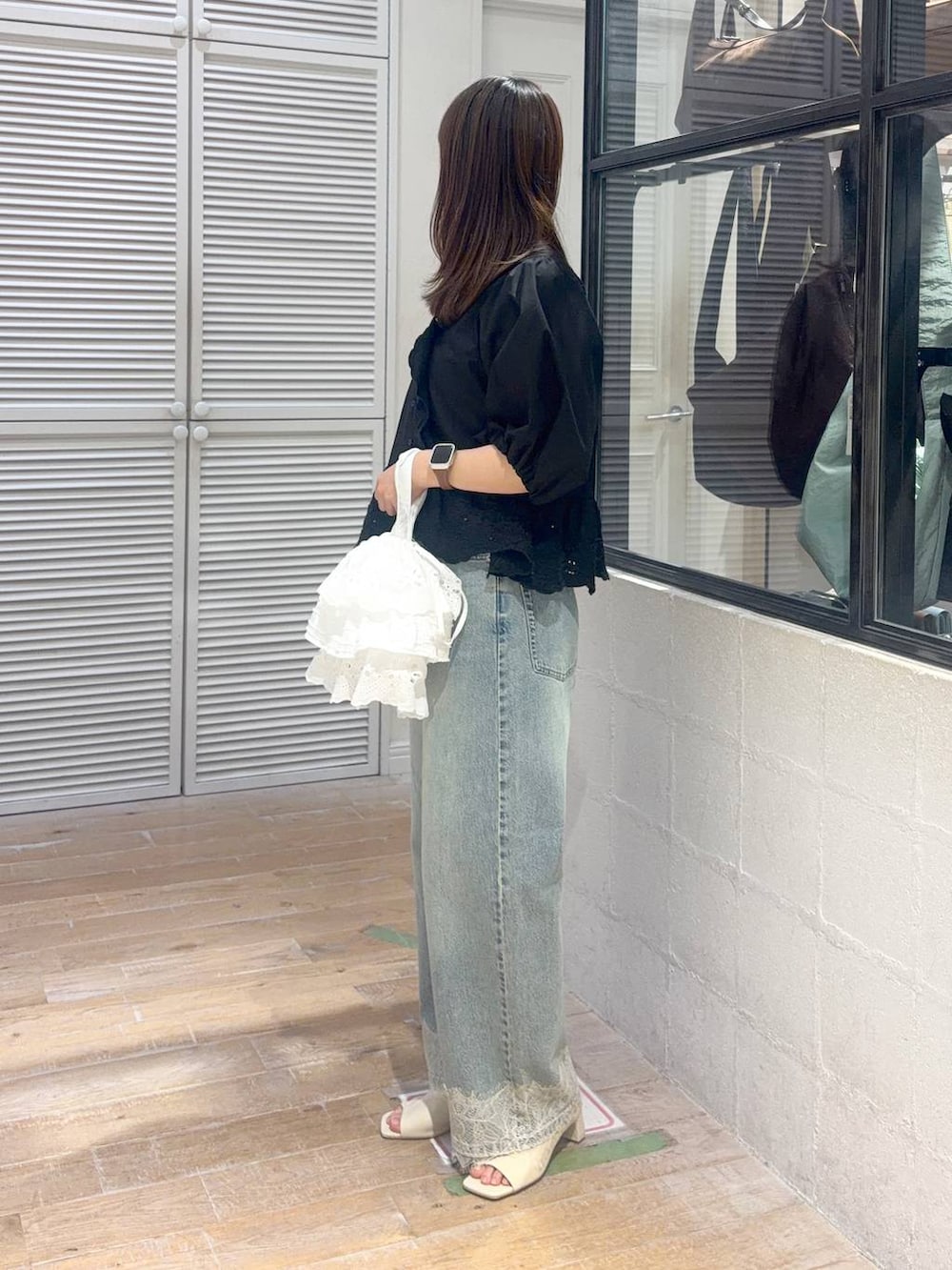 ブルー系のデニムパンツ、ブラック系のシャツ/ブラウス、ホワイト系のハンドバッグを着用したレディースの夏コーディネートの2枚目の写真