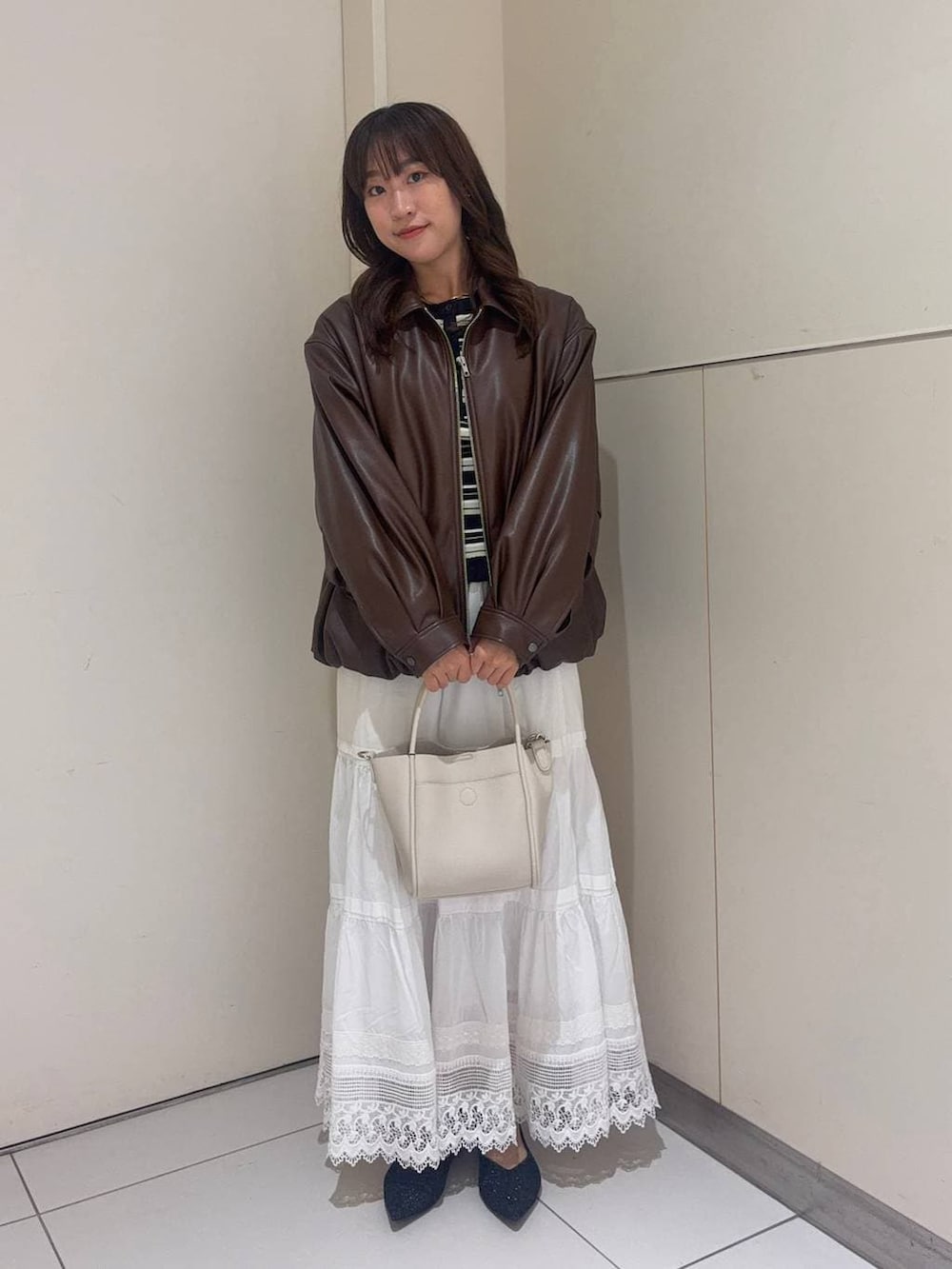 ホワイト系のショルダーバッグ、ブラック系のパンプス、ブラウン系のブルゾンを着用したレディースの春コーディネートの2枚目の写真