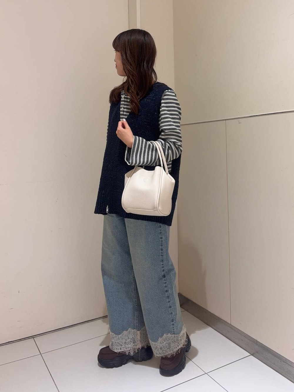 ホワイト系のショルダーバッグ、ブルー系のデニムパンツ、ブラウン系のローファーを着用したレディースの春コーディネートの2枚目の写真