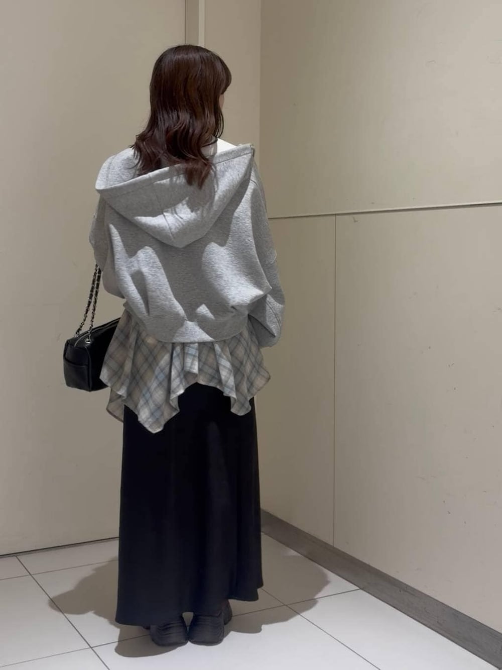 ブラック系のスカート、ホワイト系のニット/セーター、グレー系のパーカーを着用したレディースの春コーディネートの2枚目の写真