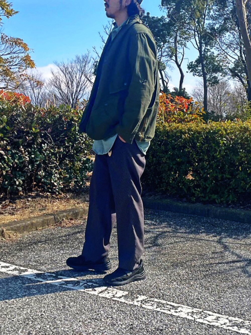 グリーン系のミリタリージャケット、グレー系のスラックス、ブラック系のスニーカーを着用したメンズの春コーディネートの2枚目の写真