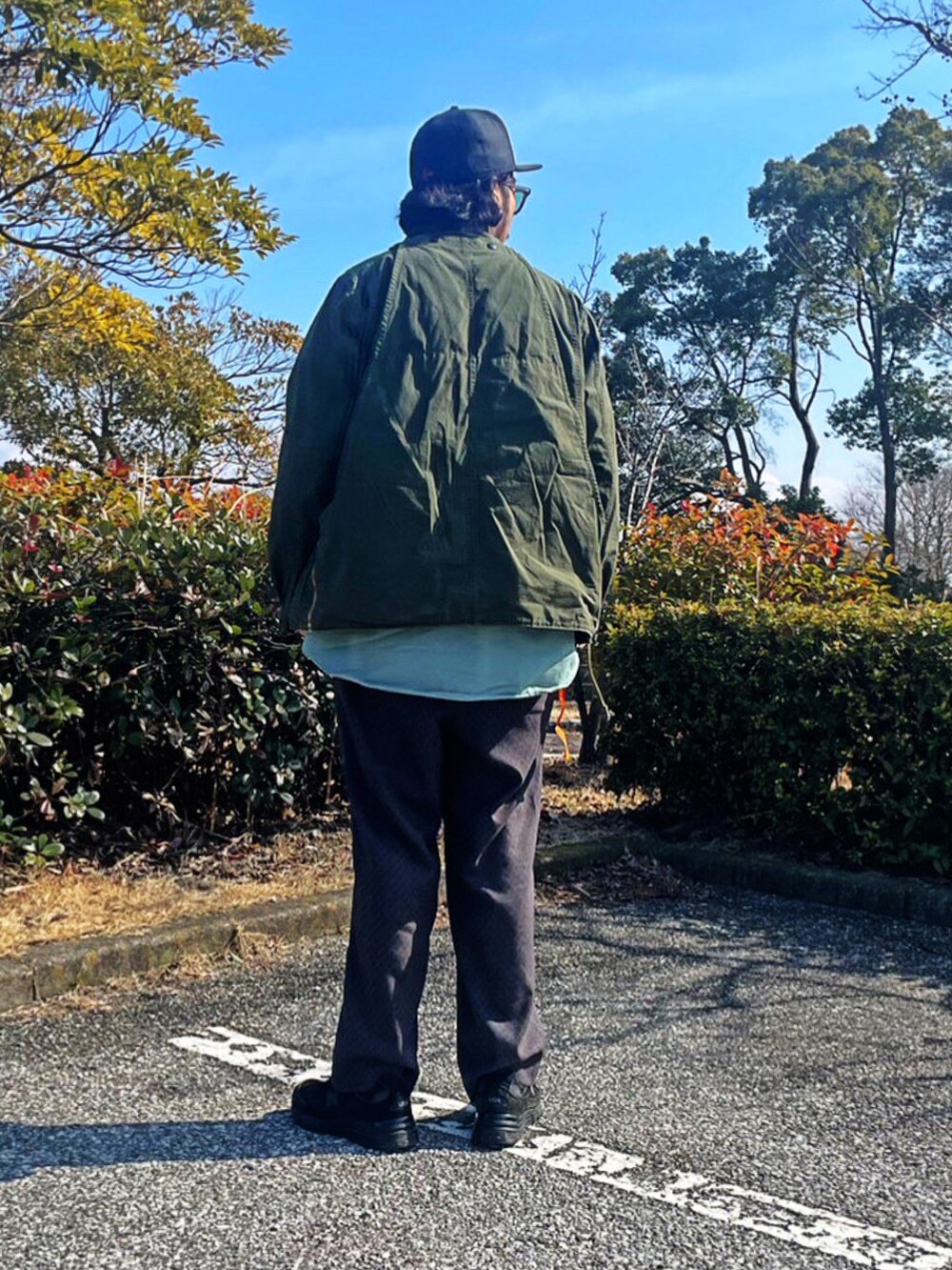 グリーン系のミリタリージャケット、グレー系のスラックス、ブラック系のスニーカーを着用したメンズの春コーディネートの3枚目の写真