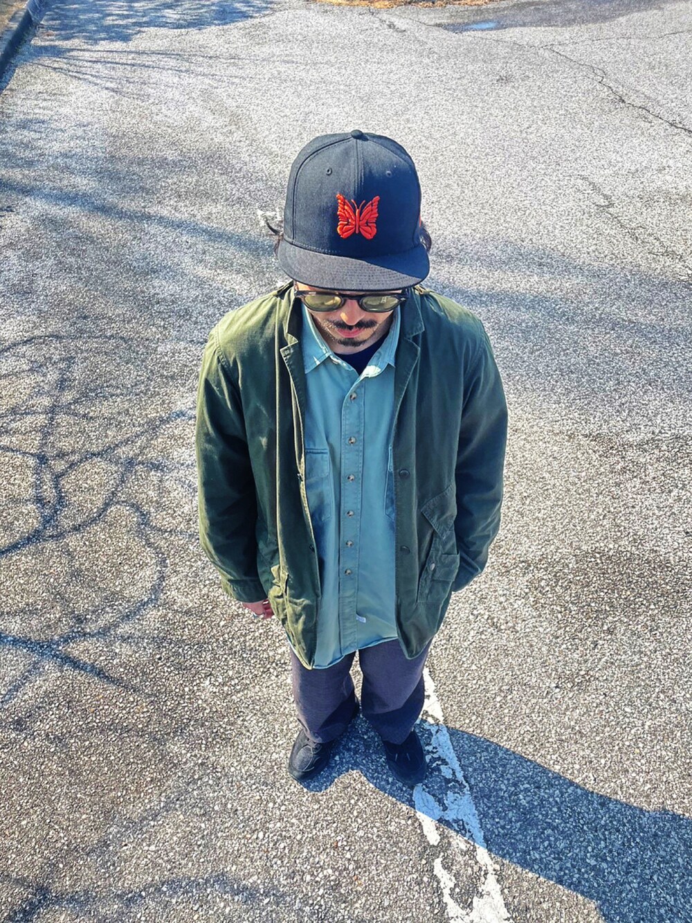 グリーン系のミリタリージャケット、グレー系のスラックス、ブラック系のスニーカーを着用したメンズの春コーディネートの5枚目の写真