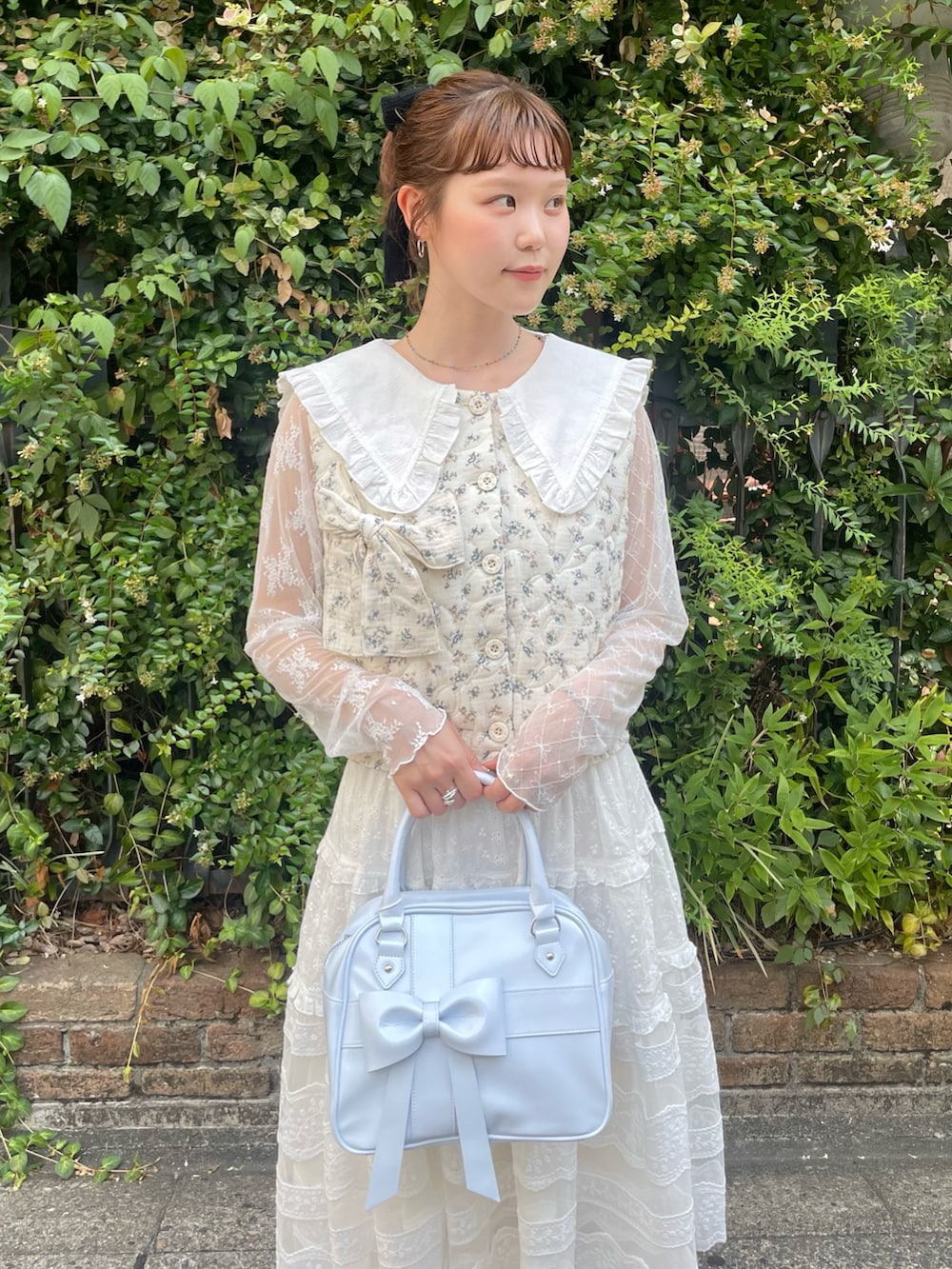 ホワイト系のスカート、ブルー系のハンドバッグ、ブルー系のベストを着用したレディースの夏コーディネートの5枚目の写真