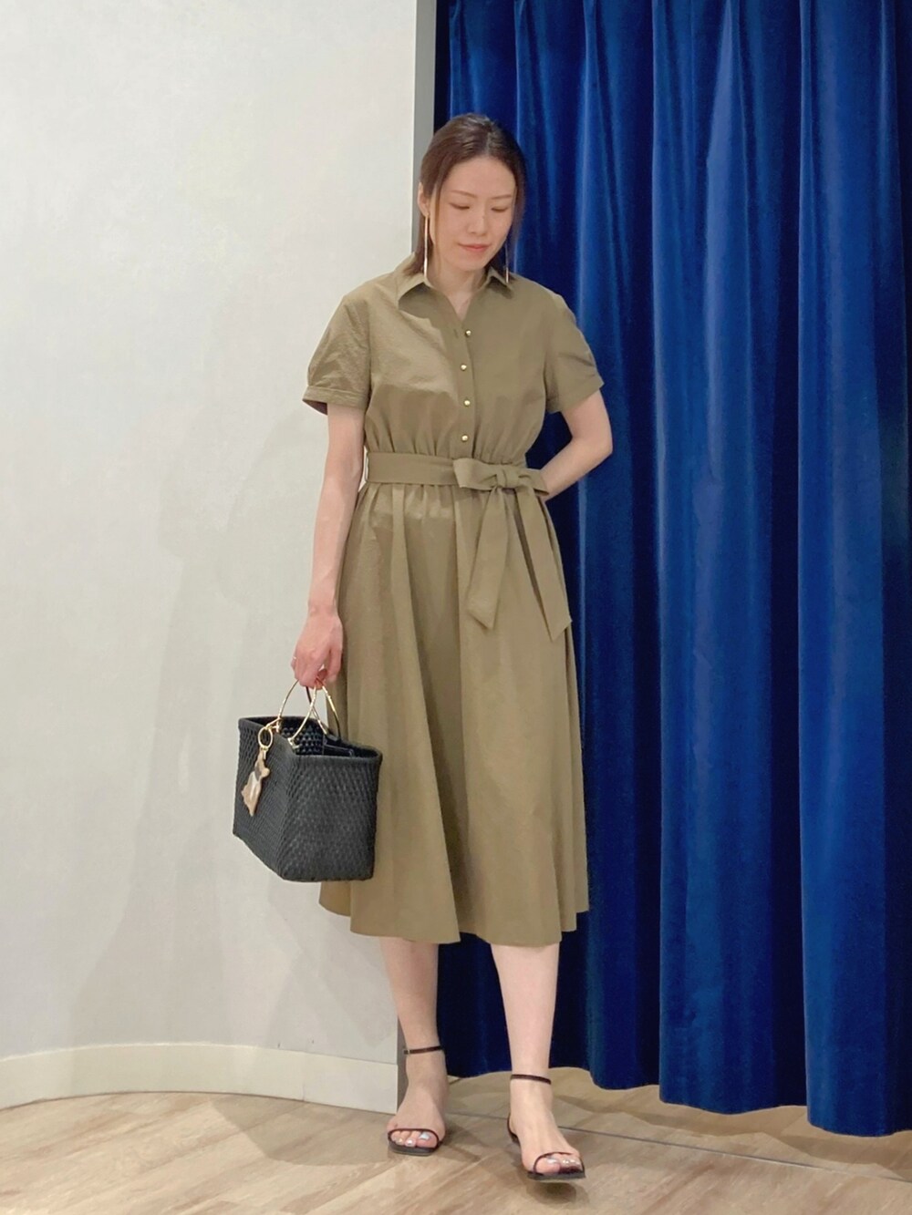 グリーン系のシャツワンピース、ブラック系のかごバッグ、ゴールド系のピアス（両耳用）を着用したレディースの夏コーディネートの3枚目の写真