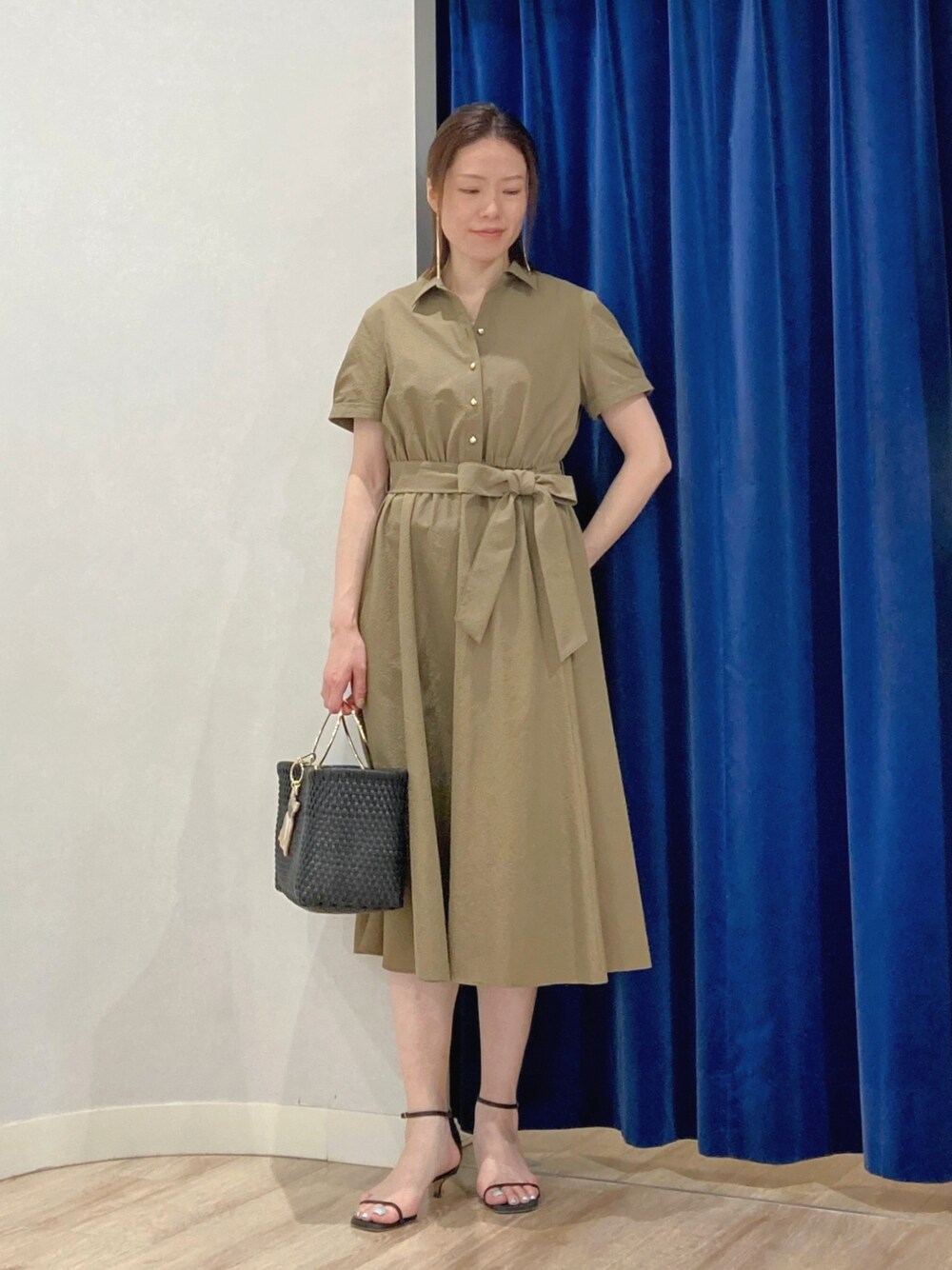 グリーン系のシャツワンピース、ブラック系のかごバッグ、ゴールド系のピアス（両耳用）を着用したレディースの夏コーディネートの2枚目の写真