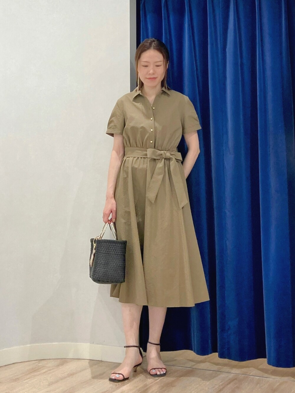 グリーン系のシャツワンピース、ブラック系のかごバッグ、ゴールド系のピアス（両耳用）を着用したレディースの夏コーディネートの7枚目の写真