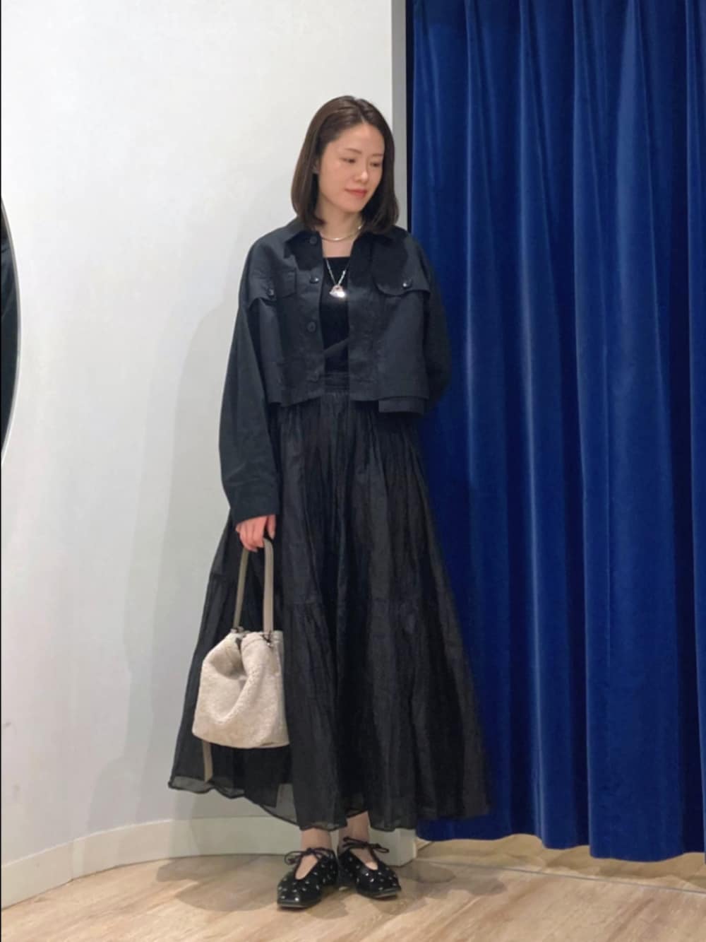 ブラック系のスカート、ブラック系のブルゾン、ベージュ系のショルダーバッグを着用したレディースの秋コーディネートの2枚目の写真