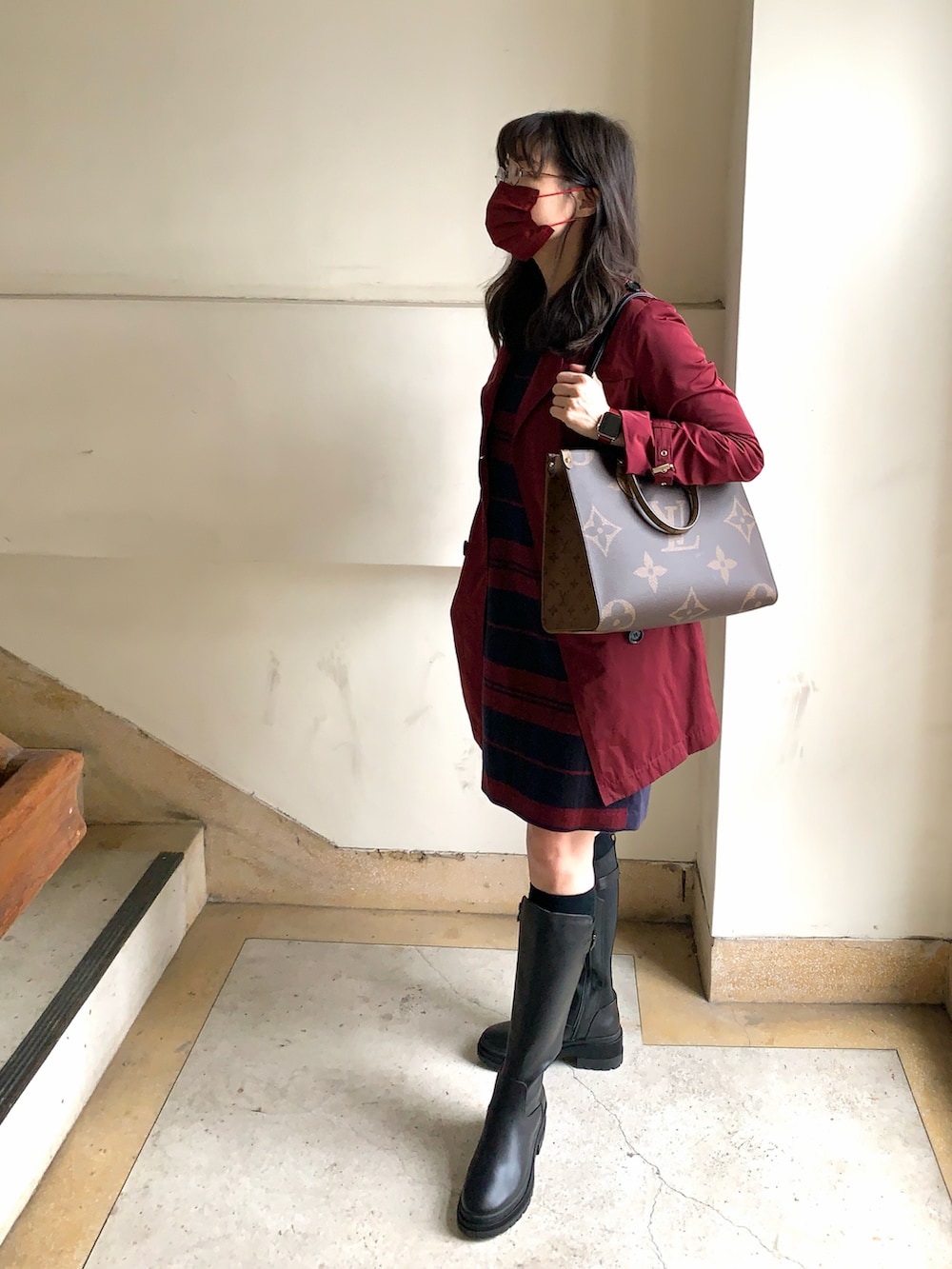 ブラウン系のショルダーバッグ、ブラック系のブーツ、レッド系のトレンチコートを着用したレディースの秋コーディネートの2枚目の写真