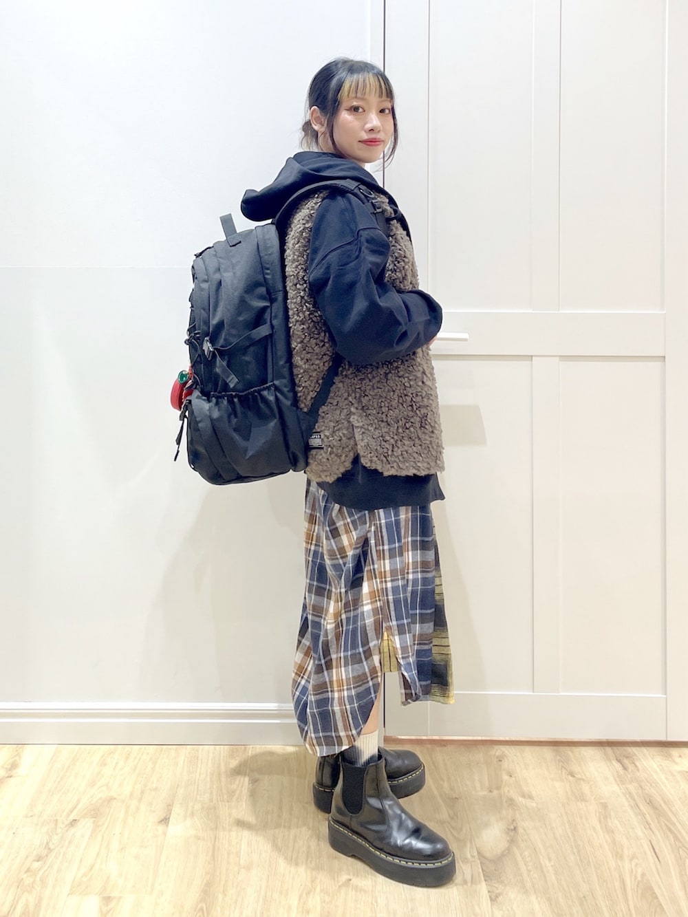 ブラウン系のベスト、イエロー系のワンピース、ブラック系のブーツを着用したレディースの冬コーディネートの2枚目の写真