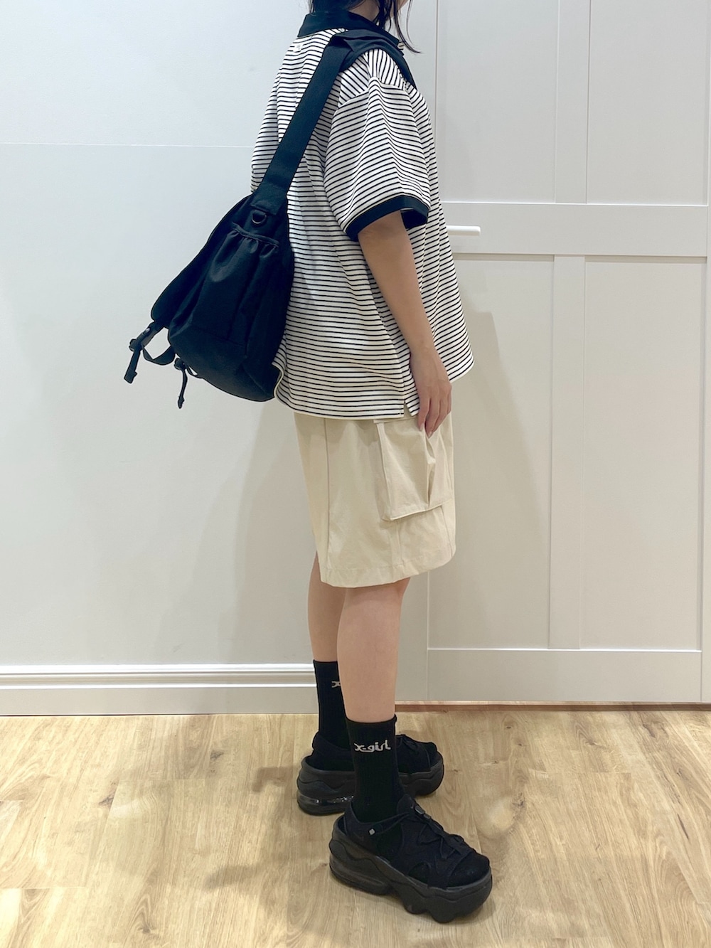 ホワイト系のポロシャツ、ブラック系のメッセンジャーバッグ、ブラック系のサンダルを着用したレディースの春コーディネートの2枚目の写真