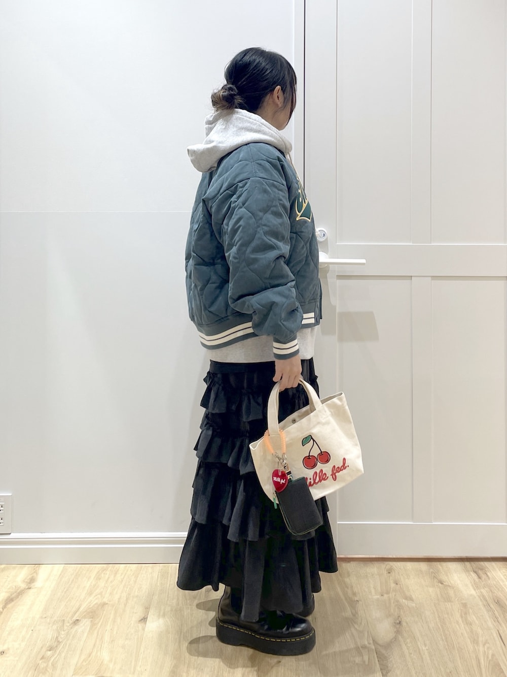 グレー系のパーカー、ブラック系のスカート、グリーン系のスタジャンを着用したレディースの冬コーディネートの4枚目の写真