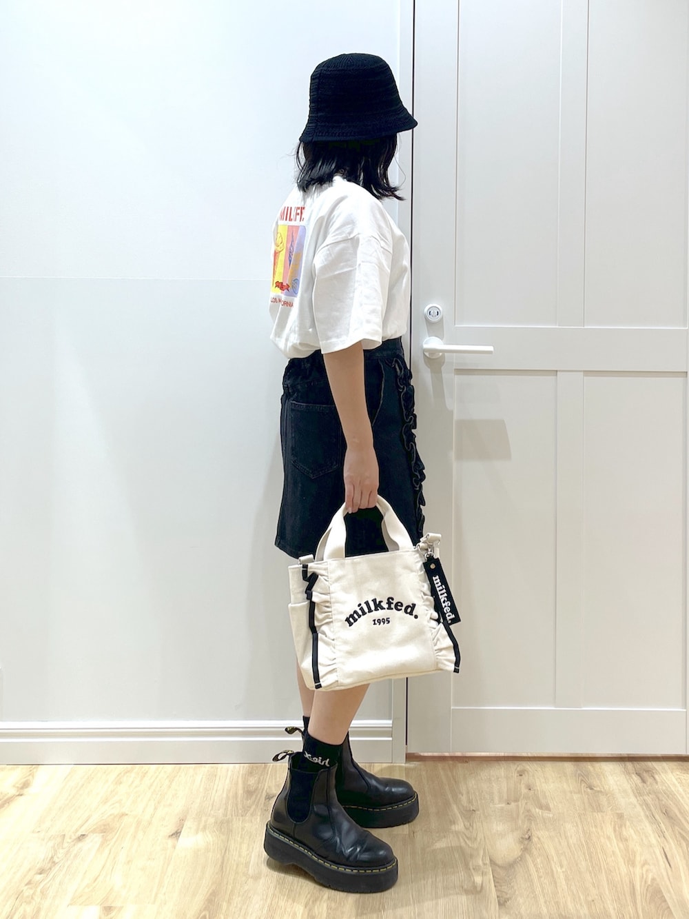 ホワイト系のショルダーバッグ、ブラック系のブーツ、ブラック系のデニムスカートを着用したレディースの夏コーディネートの3枚目の写真