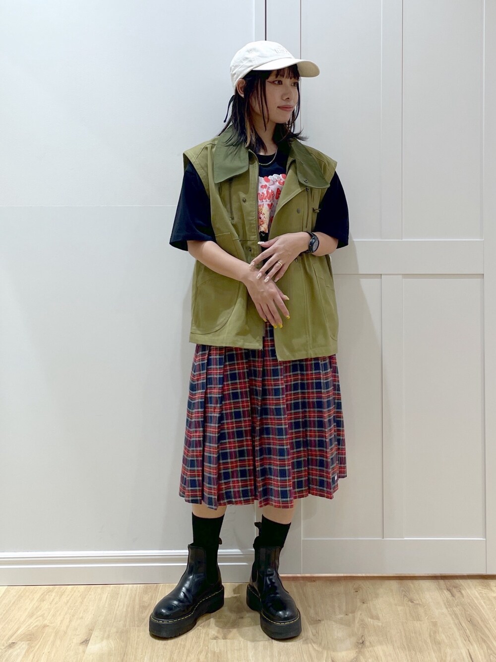 ブラック系のブーツ、ブルー系のスカート、グリーン系のベストを着用したレディースの秋コーディネートの2枚目の写真