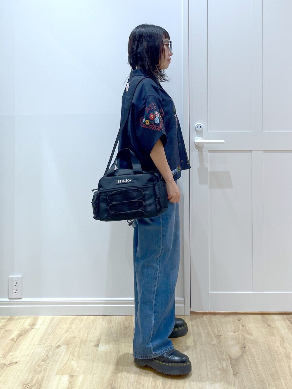 ブルー系のデニムパンツ、ブラック系のブーツ、レッド系のショルダーバッグを着用したレディースの夏コーディネートの2枚目の写真