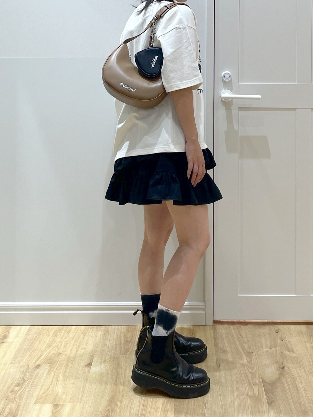 ブラック系のスカート、ホワイト系のTシャツ/カットソー、ブラック系のブーツを着用したレディースの夏コーディネートの4枚目の写真