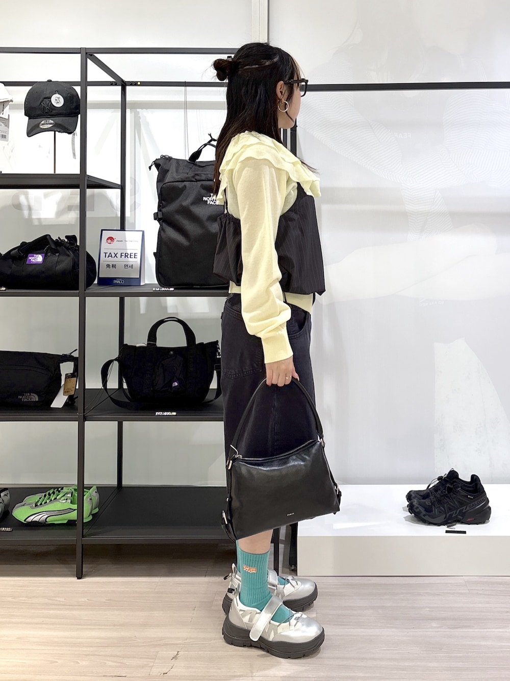 シルバー系のスニーカー、ブラック系のハンドバッグ、ブラック系のデニムパンツを着用したレディースの春コーディネートの3枚目の写真