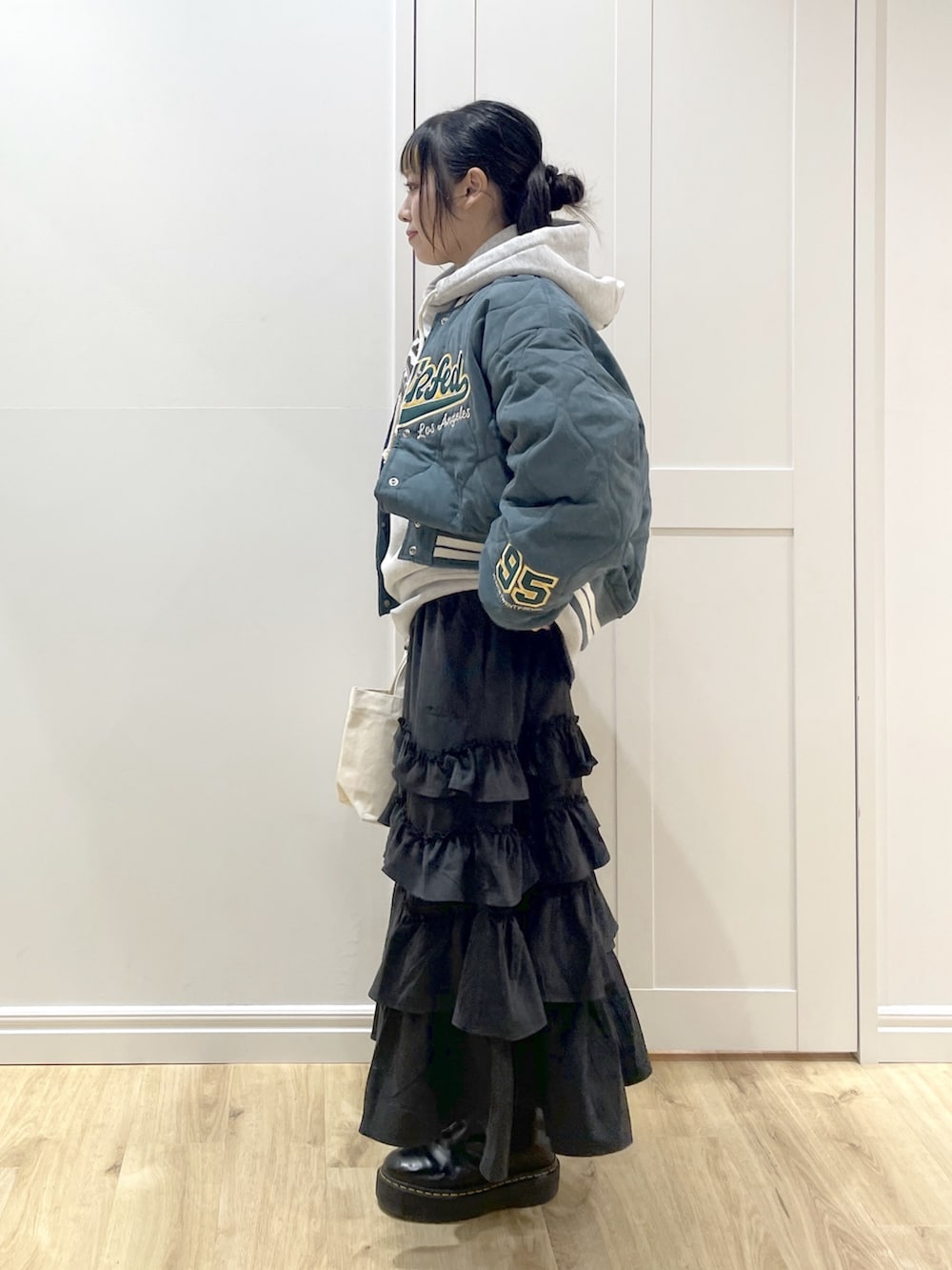 グレー系のパーカー、ブラック系のスカート、グリーン系のスタジャンを着用したレディースの冬コーディネートの2枚目の写真