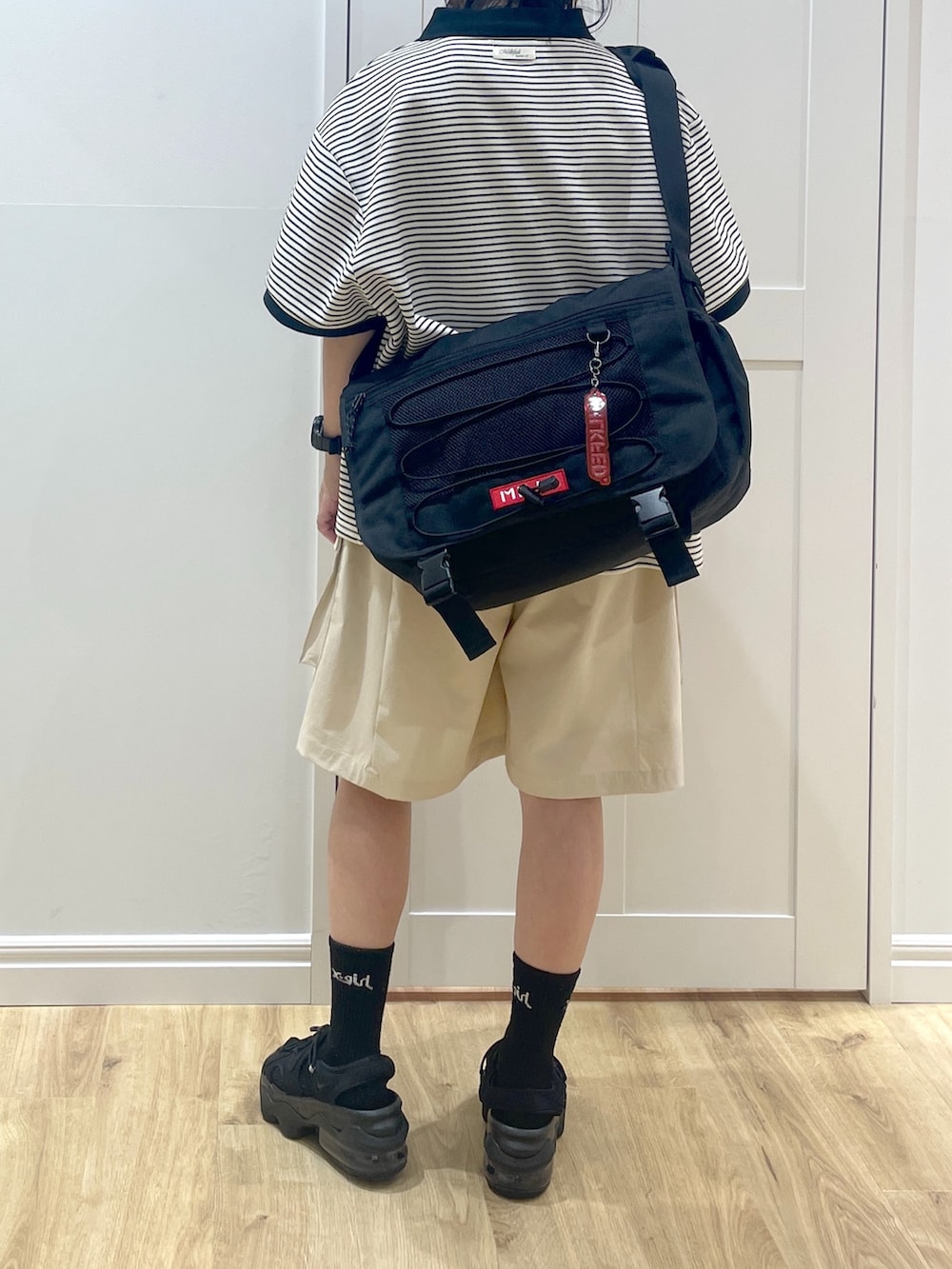 ホワイト系のポロシャツ、ブラック系のメッセンジャーバッグ、ブラック系のサンダルを着用したレディースの春コーディネートの3枚目の写真