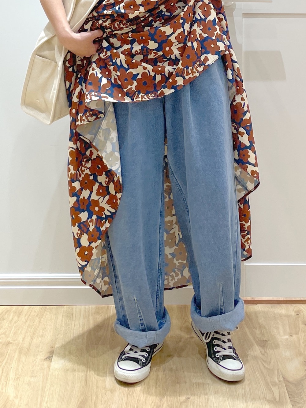 ブラウン系のワンピース、ブルー系のデニムパンツ、ブラック系のスニーカーを着用したレディースの春コーディネートの4枚目の写真