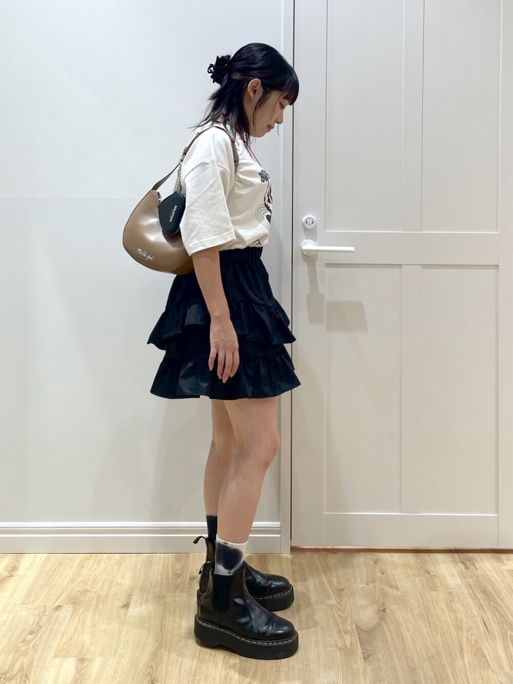 ブラック系のスカート、ホワイト系のTシャツ/カットソー、ブラック系のブーツを着用したレディースの夏コーディネートの3枚目の写真