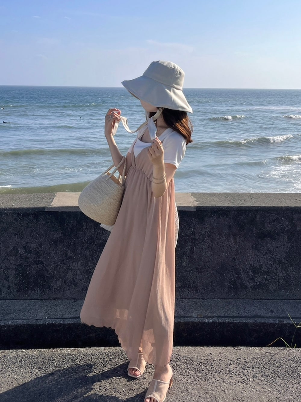 ピンク系のワンピース/ドレス、ベージュ系のバッグ、ホワイト系のハットを着用したレディースの夏コーディネートの2枚目の写真