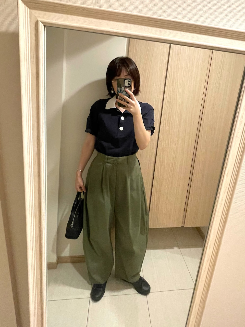 ブルー系のポロシャツ、グリーン系のチノパンツ、ブラック系のハンドバッグを着用したレディースの秋コーディネートの2枚目の写真