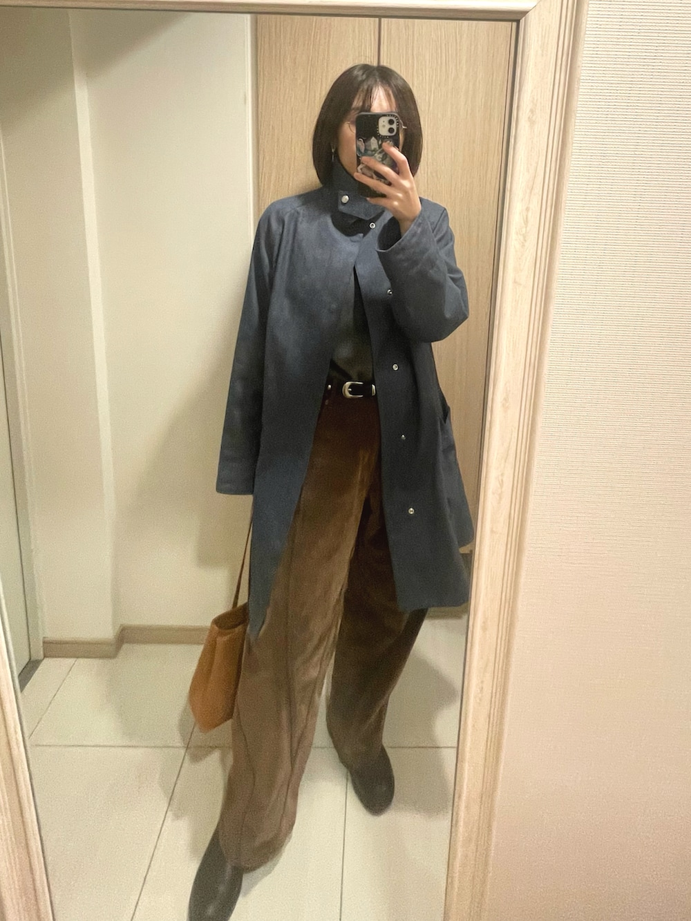 ブルー系のトレンチコート、ブラウン系のパンツ、イエロー系のハンドバッグを着用したレディースの冬コーディネートの3枚目の写真