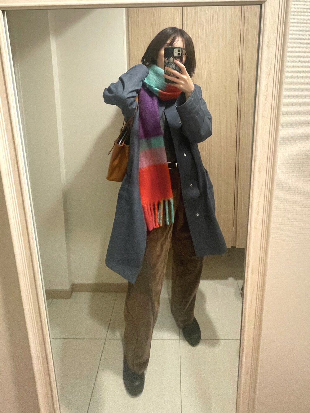 ブルー系のトレンチコート、ブラウン系のパンツ、イエロー系のハンドバッグを着用したレディースの冬コーディネートの2枚目の写真