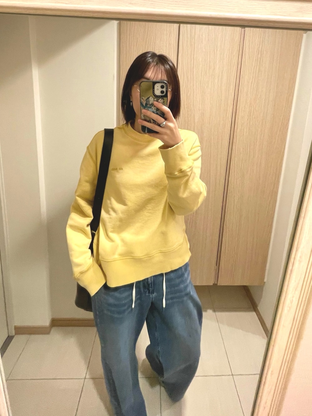 イエロー系のスウェット、ブルー系のデニムパンツ、ホワイト系のスニーカーを着用したレディースの秋コーディネートの2枚目の写真