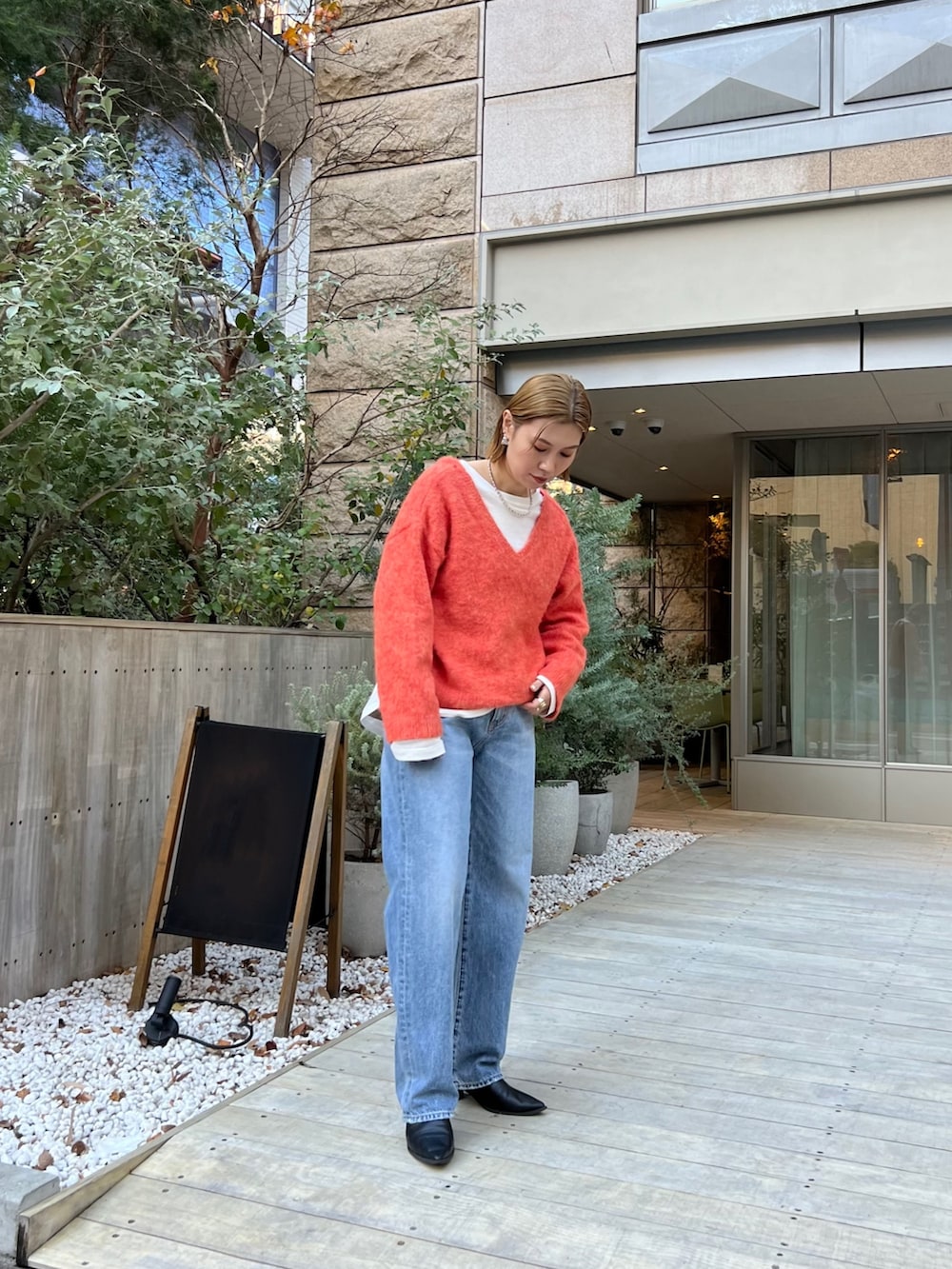 オレンジ系のニット/セーター、ホワイト系のTシャツ/カットソー、ブルー系のデニムパンツを着用したレディースの冬コーディネートの2枚目の写真