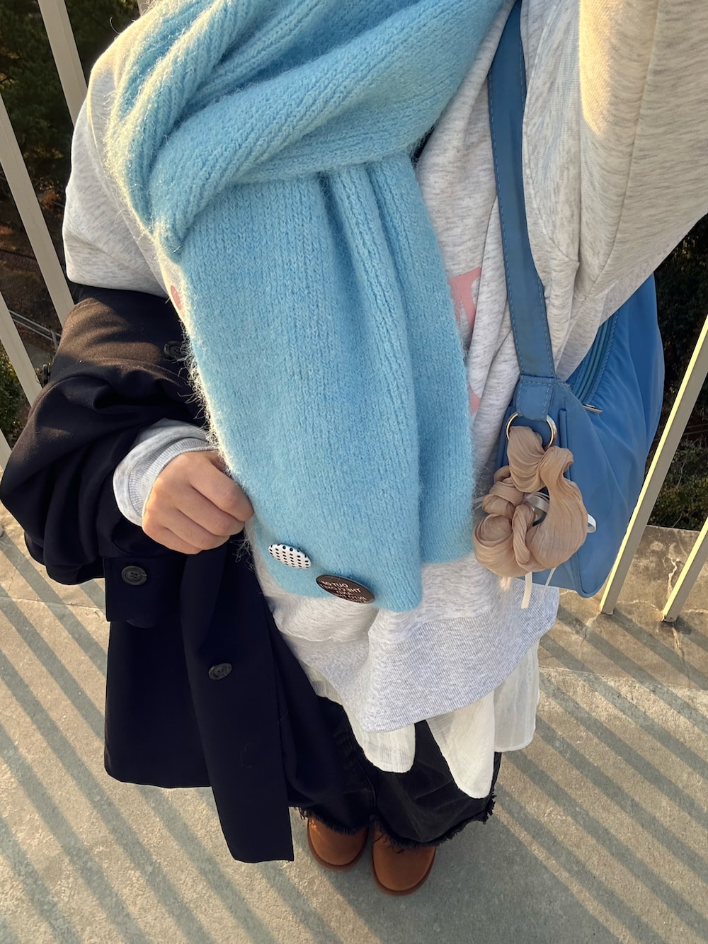 グレー系のパーカー、ブルー系のハンドバッグ、ブルー系のマフラーを着用したレディースの冬コーディネートの2枚目の写真