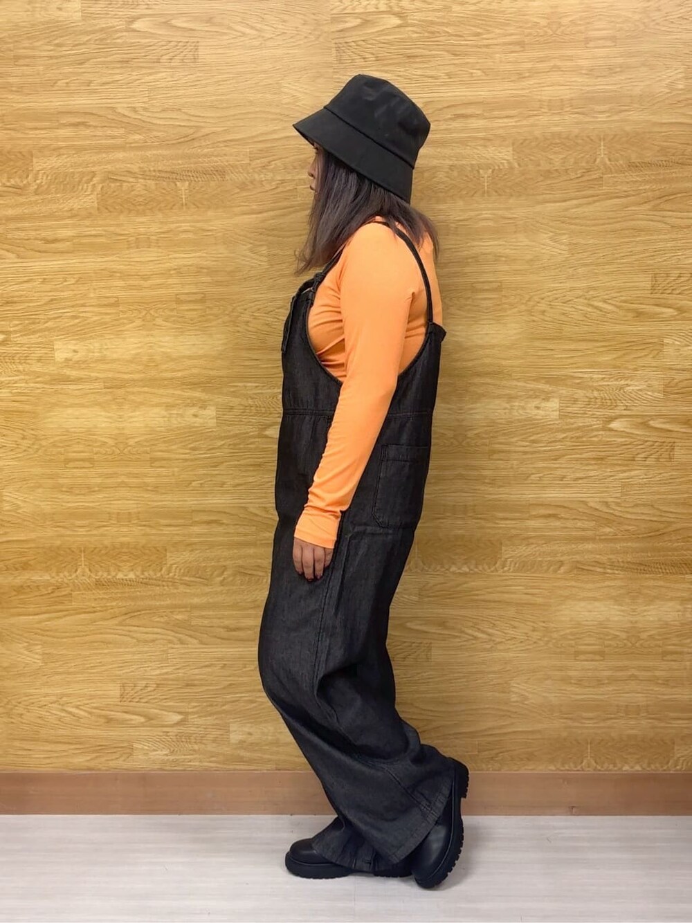 オレンジ系のTシャツ/カットソー、ブラック系のサロペット/オーバーオール、ブラック系のブーツを着用したレディースの秋コーディネートの2枚目の写真