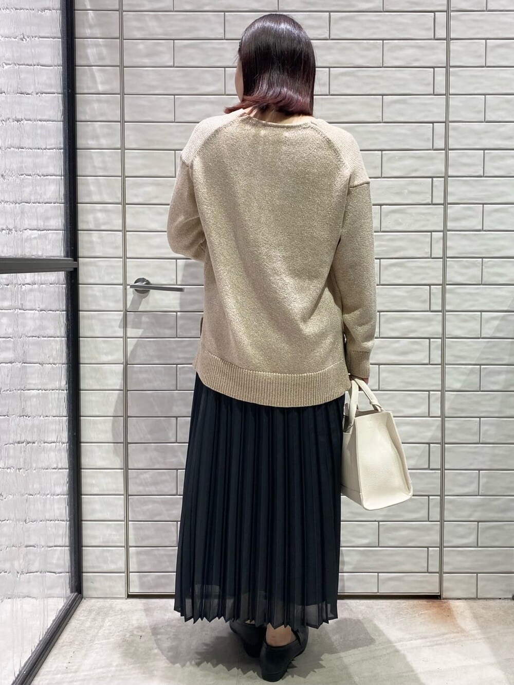 オレンジ系のニット/セーター、グレー系のスカート、ホワイト系のトートバッグを着用したレディースの冬コーディネートの2枚目の写真