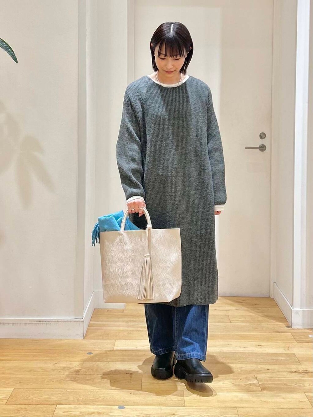 ホワイト系のトートバッグ、ブルー系のデニムパンツ、ブラック系のブーツを着用したレディースの冬コーディネートの2枚目の写真