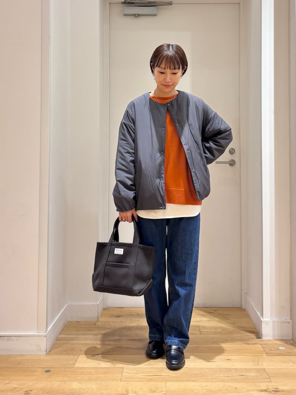 グレー系のブルゾン、オレンジ系のニット/セーター、ホワイト系のTシャツ/カットソーを着用したレディースの秋コーディネートの3枚目の写真