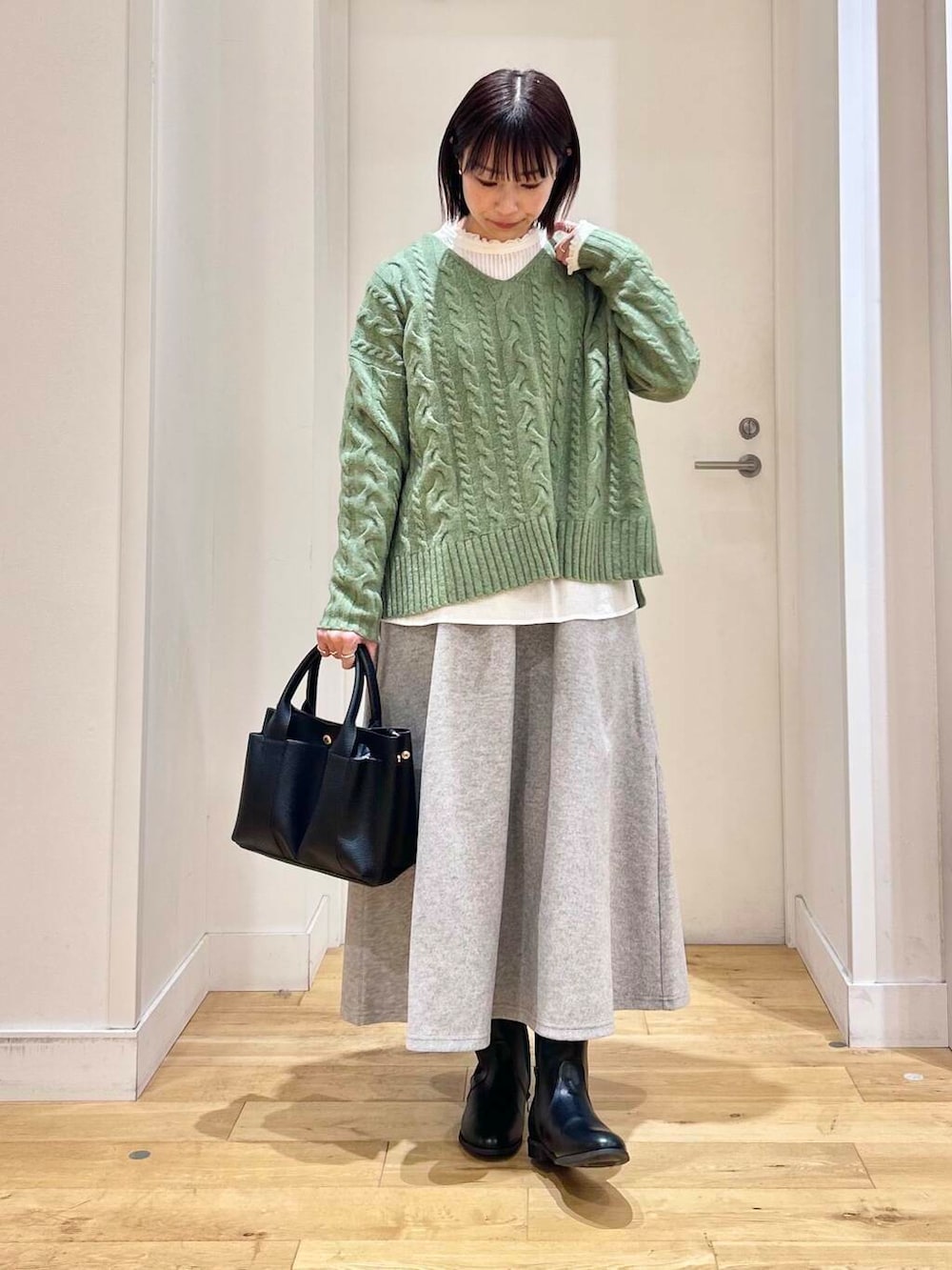 グリーン系のニット/セーター、ホワイト系のシャツ/ブラウス、ブラック系のブーツを着用したレディースの冬コーディネートの2枚目の写真