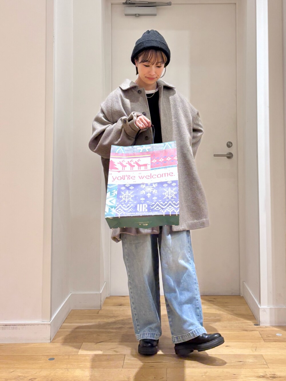 グレー系のステンカラーコート、ブルー系のデニムパンツ、ブラック系のブーツを着用したレディースの秋コーディネートの5枚目の写真